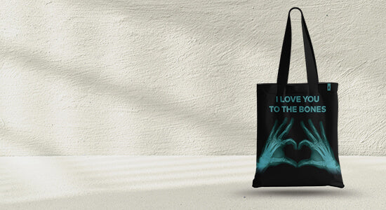 Tote bag negra con impresión de manos esqueléticas en forma de corazón, con el mensaje 'I Love You To The Bones'.