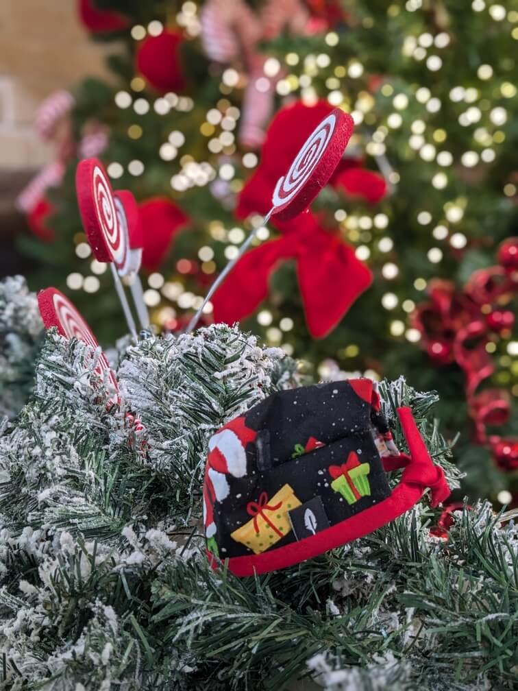 Gorro quirúrgico negro con estampado de regalos y motivos navideños, rodeado de nieve artificial y decoraciones festivas.