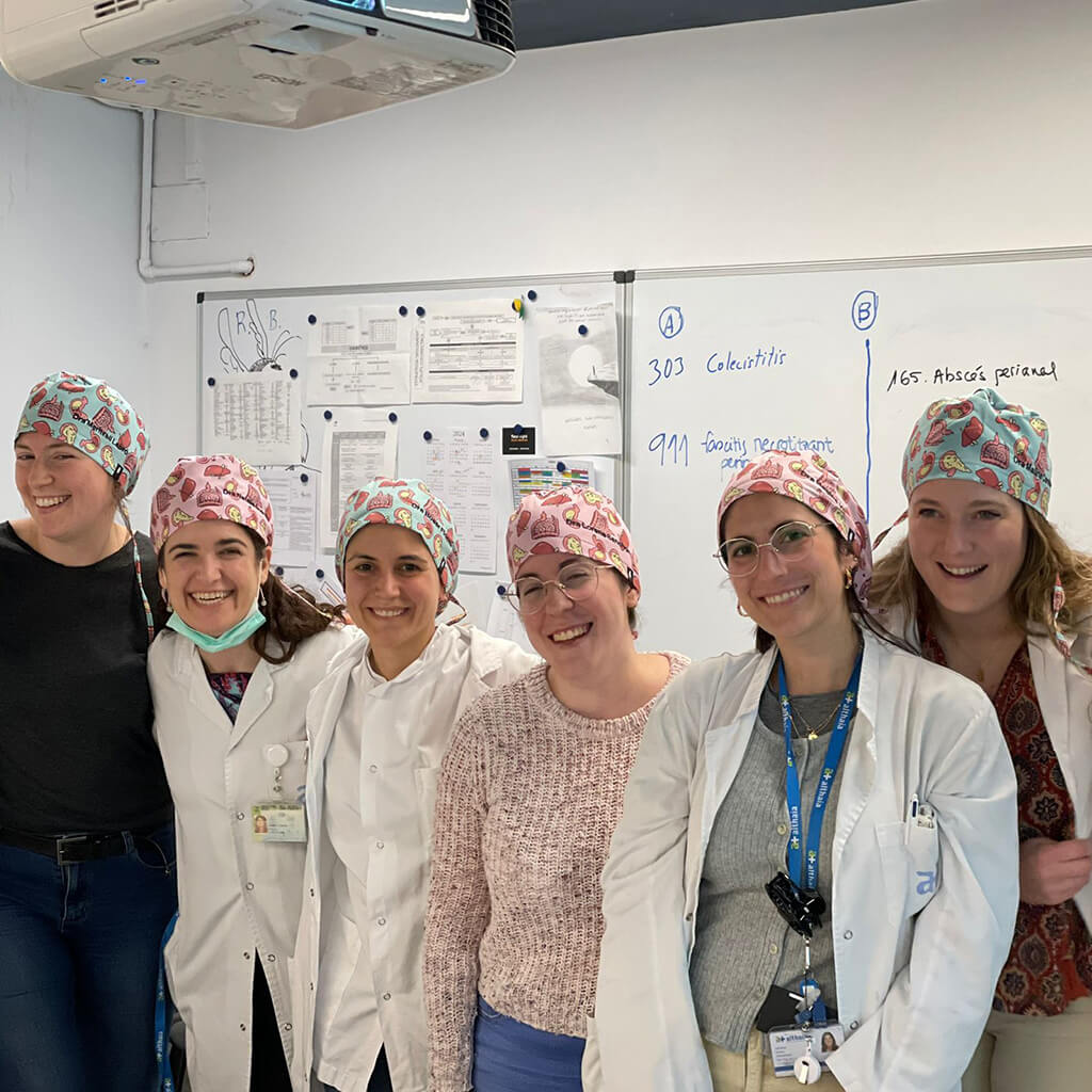 Seis profesionales sanitarias sonriendo en hospital usando gorro quirúrgico DIGESTIVE Robin Hat con diseños del aparato digestivo, especializado para gastroenterología, batas blancas