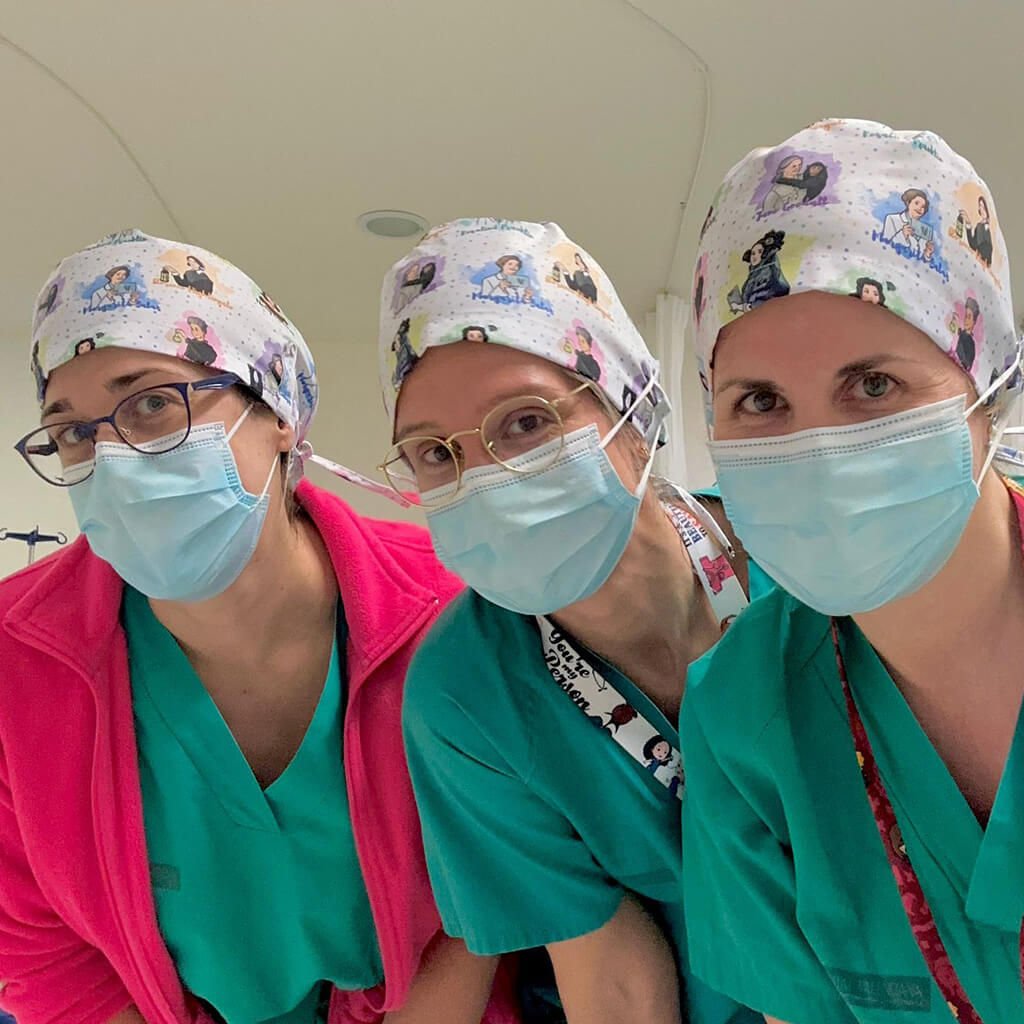 Tres profesionales sanitarias en quirófano usando gorro quirúrgico MUJERES DE LA HISTORIA Robin Hat con ilustraciones de Marie Curie, Frida Kahlo, Dian Fossey y Amelia Earhart, mascarillas azules