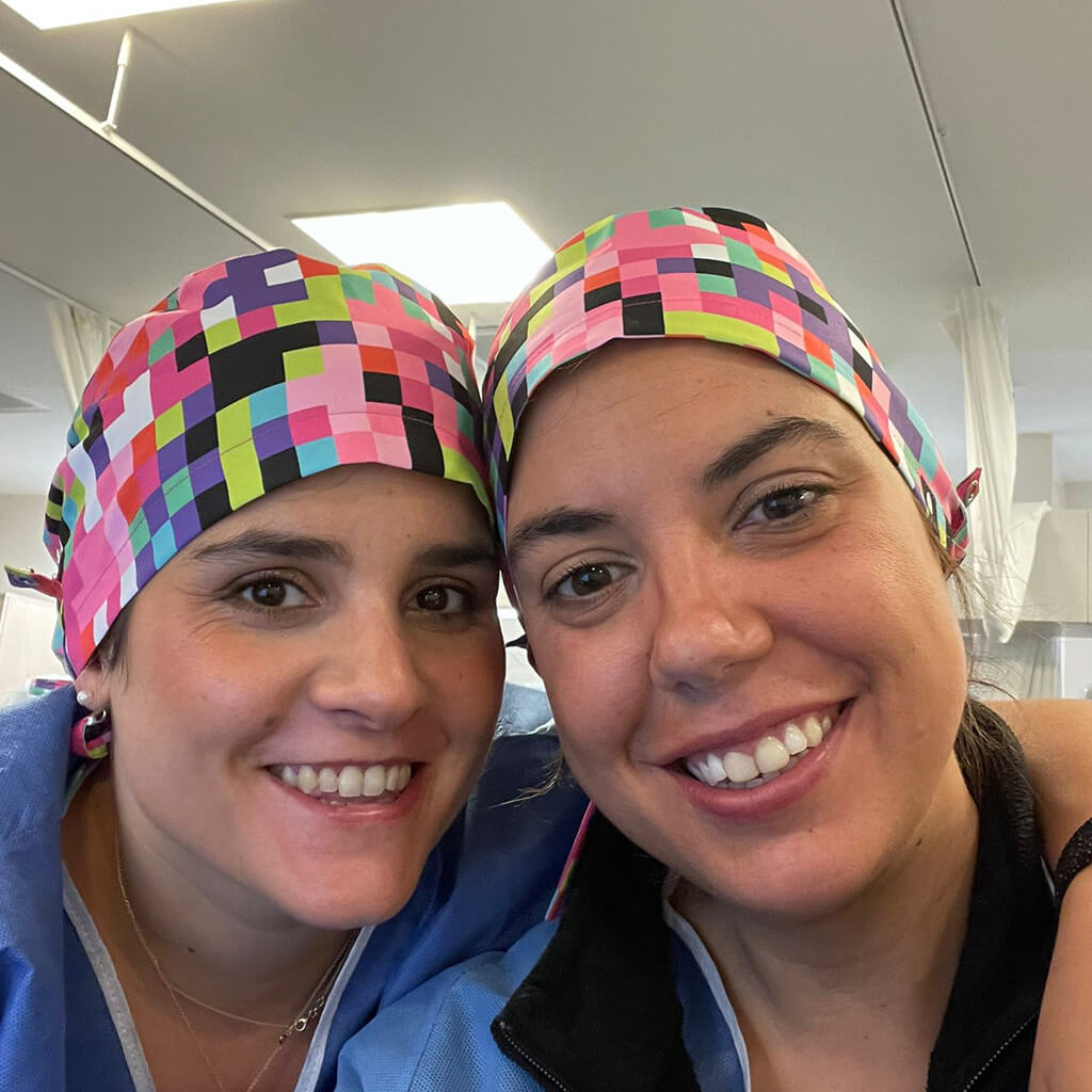 Dos profesionales sanitarias sonriendo en hospital usando gorro quirúrgico PIXEL ROSA Robin Hat con diseño de cuadros multicolores tipo pixel, fabricado en España