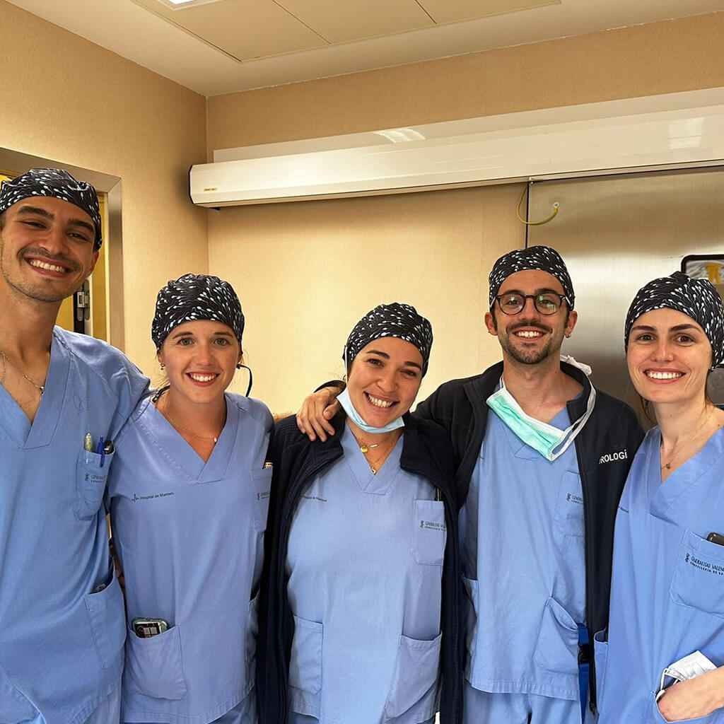 Cinco profesionales sanitarios sonriendo en hospital usando gorro quirúrgico RUN Robin Hat negro con patrón, uniformes azules, equipo médico mixto
