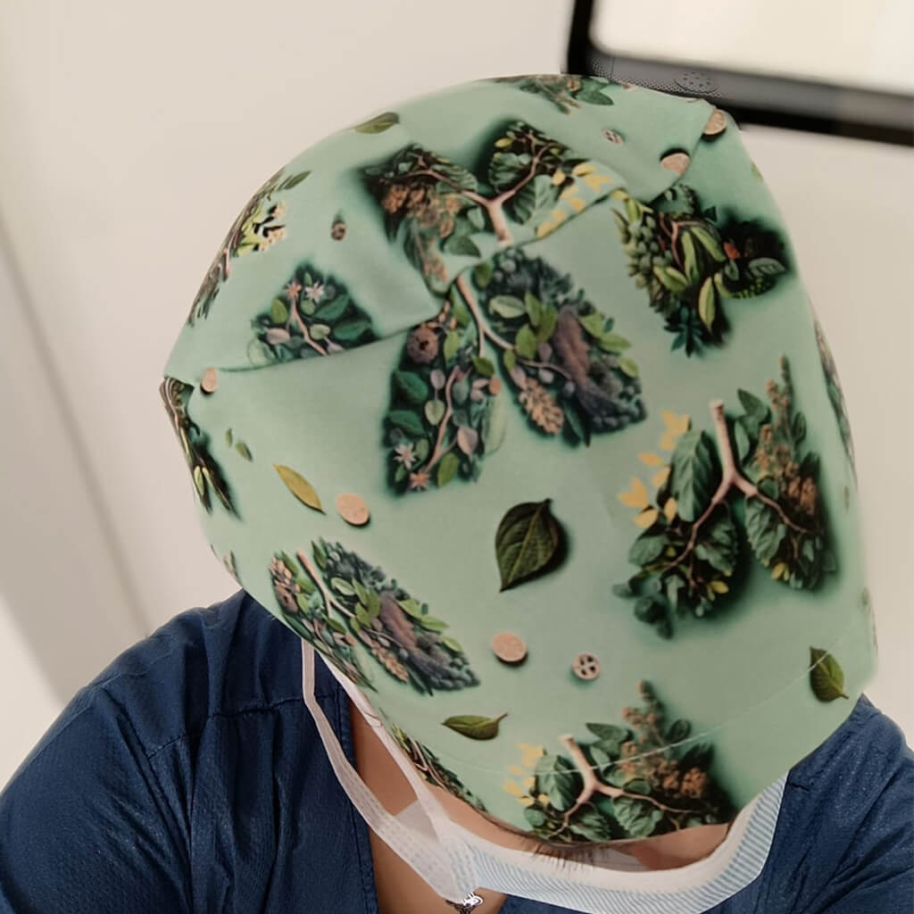Vista posterior del gorro quirúrgico BREATHE Robin Hat en color verde con diseño de pulmones formados por hojas y árboles, usado por enfermera en hospital mostrando el estampado completo especializado en neumología