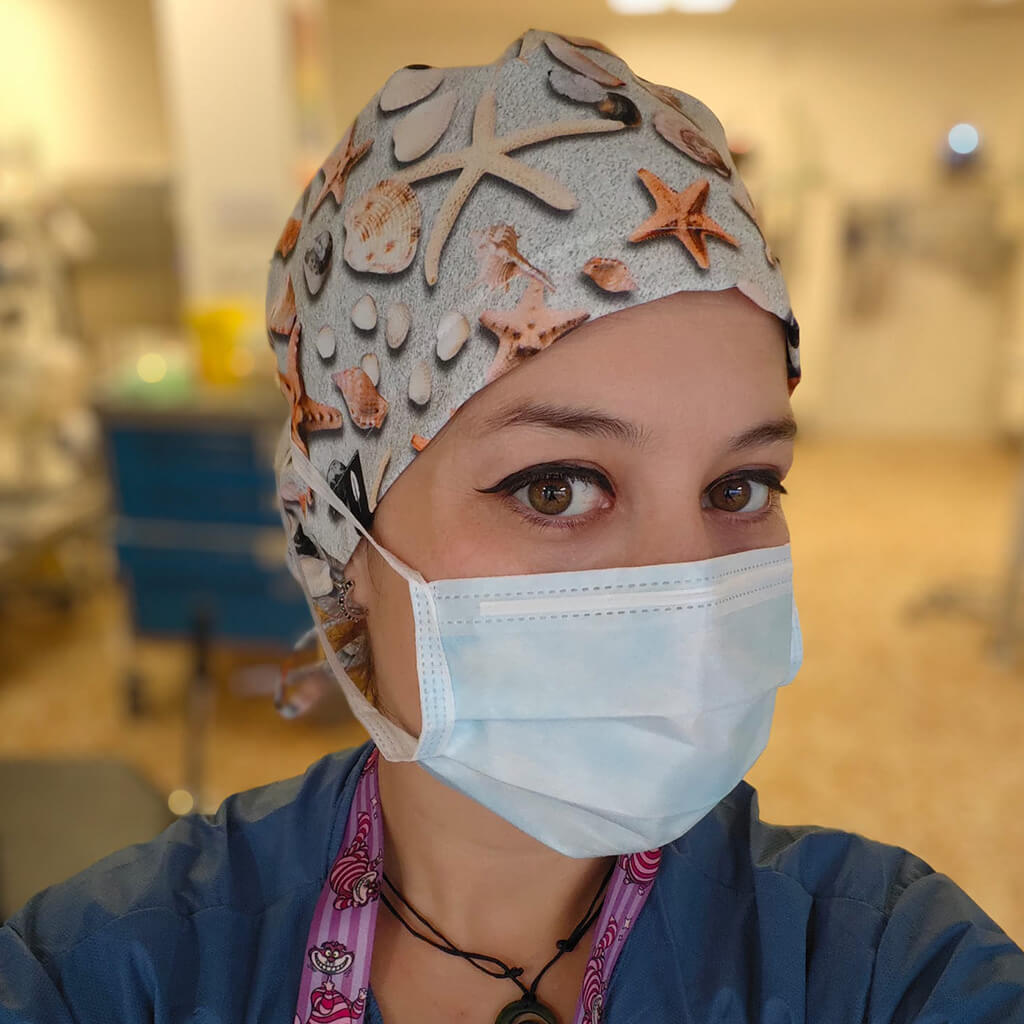 Enfermera en hospital usando gorro quirúrgico ESTRELLAS MAR de Robin Hat con diseño marino de estrellas de mar, conchas y elementos del océano sobre fondo gris, llevando mascarilla durante jornada laboral hospitalaria con temática del mar