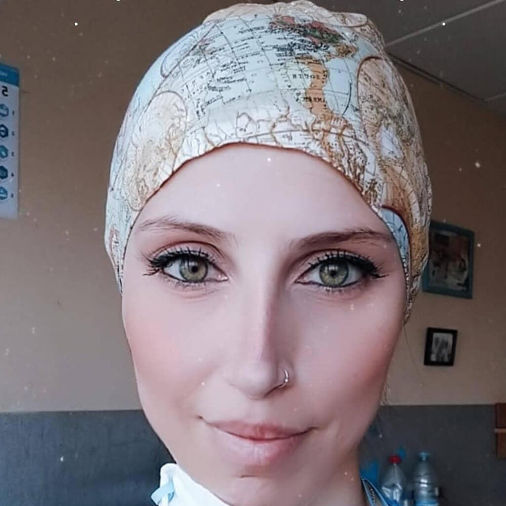 Enfermera sonriendo en hospital usando gorro quirúrgico MAGALLANES de Robin Hat con diseño de mapas antiguos inspirado en Fernando de Magallanes, confeccionado en algodón suave con toque histórico y aventurero para largas jornadas laborales