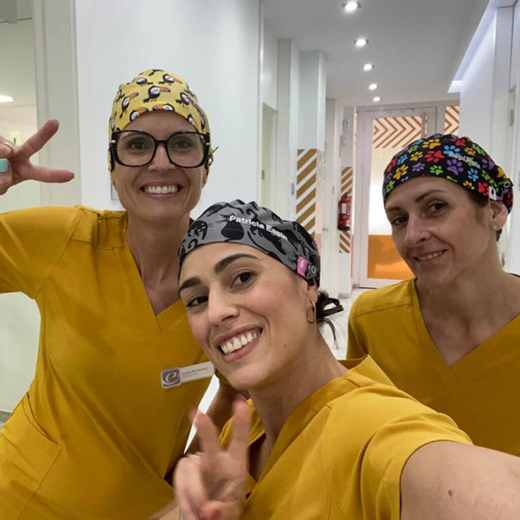 Equipo de tres profesionales sanitarias con uniformes amarillos tomándose selfie usando gorros quirúrgicos TUKI TUKI de Robin Hat con diseño de tucanes tropicales sobre fondo amarillo confeccionados en algodón durante jornada laboral en centro médico con ambiente amigable