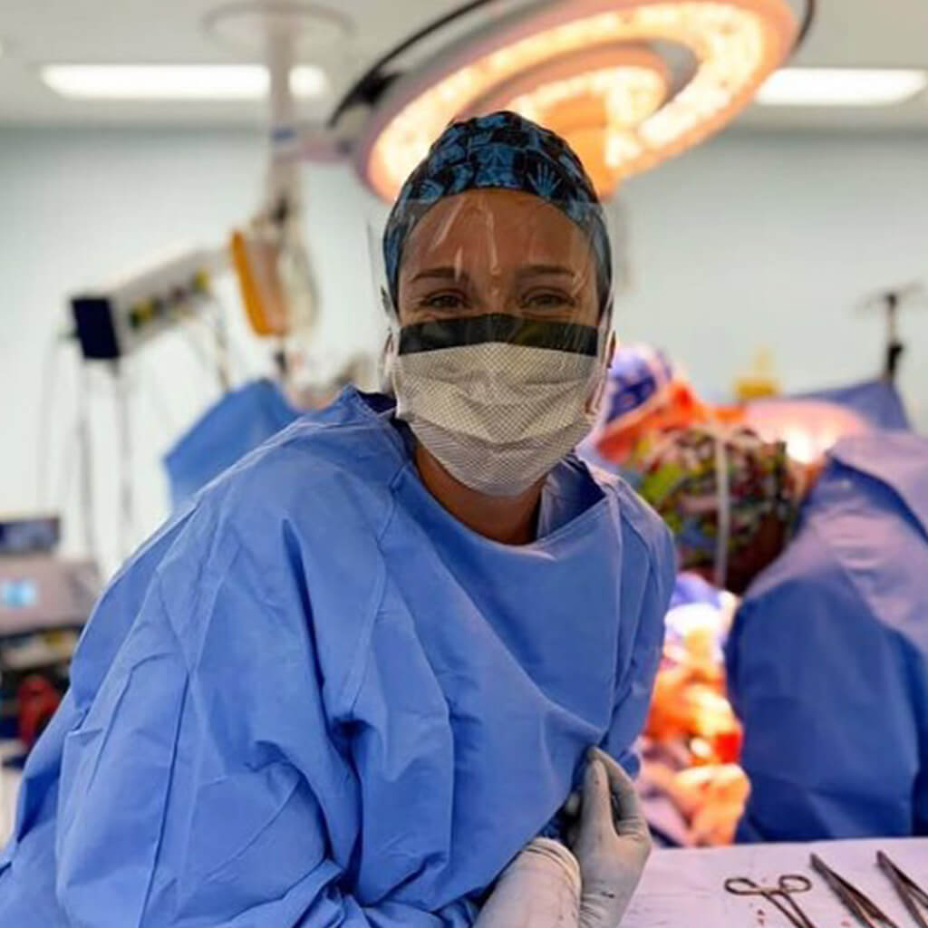 Cirujana en quirofano activo con lampara cialtica y gorro Robin Hat modelo X-Ray, patron azul oscuro con motivos de rayos X y esqueletos, diseño para radiologos traumatologos y especialistas quirurgicos