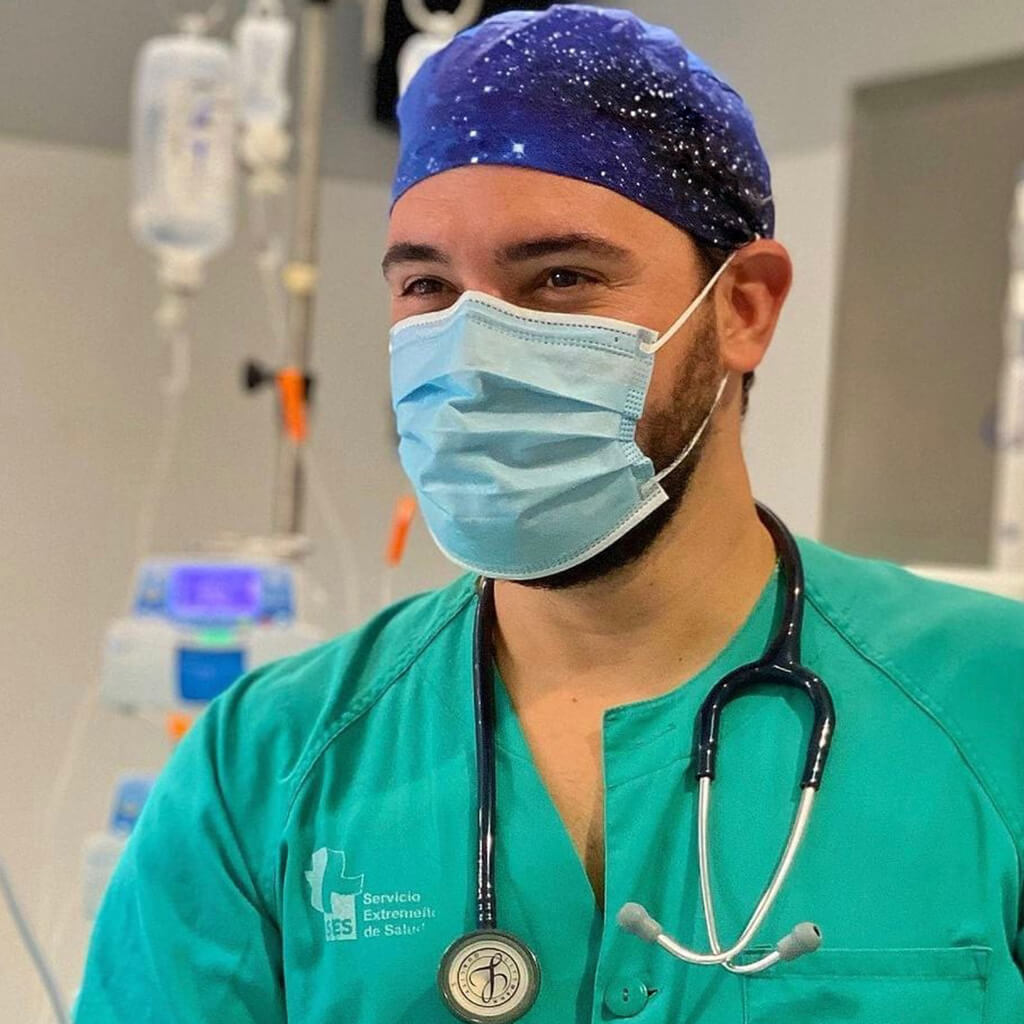 Médico del Servicio Extremeño de Salud usando gorro quirúrgico AGATHE de Robin Hat con diseño de galaxias y estrellas en tonos oscuros en quirófano hospitalario, llevando mascarilla y estetoscopio durante jornada laboral sanitaria