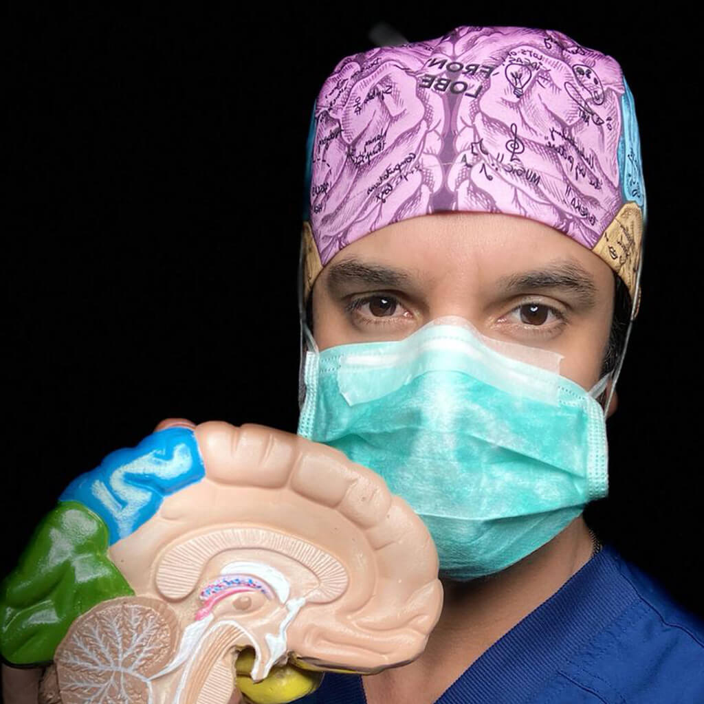 Neurocirujano usando gorro quirúrgico BRAIN de Robin Hat especializado en neurología con diseño detallado de lóbulos cerebrales, sosteniendo modelo anatómico de cerebro y llevando mascarilla durante práctica médica confeccionado en poliéster transpirable