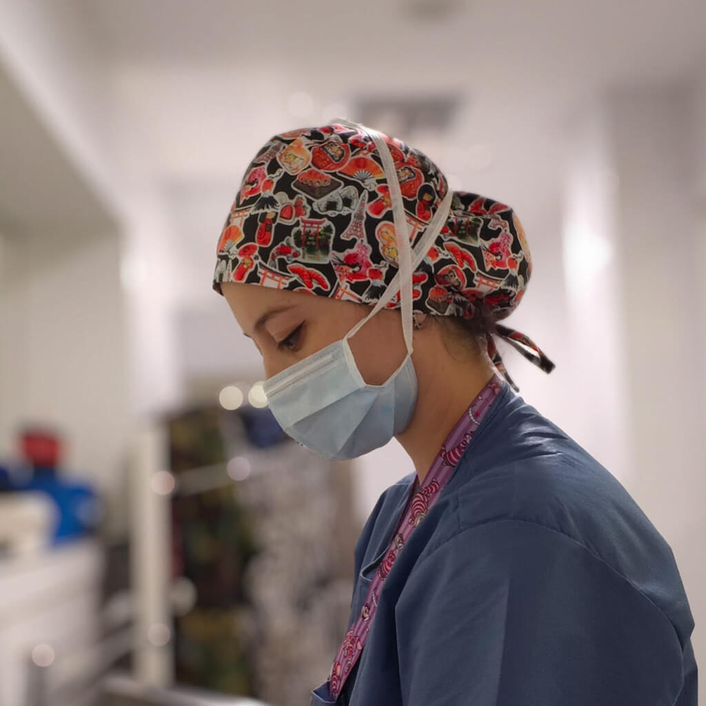 Profesional sanitaria en quirófano usando gorro quirúrgico JAPAN STICKERS de Robin Hat con diseño colorido de anime japonés y stickers, llevando mascarilla y uniforme azul durante jornada laboral hospitalaria con estilo japonés