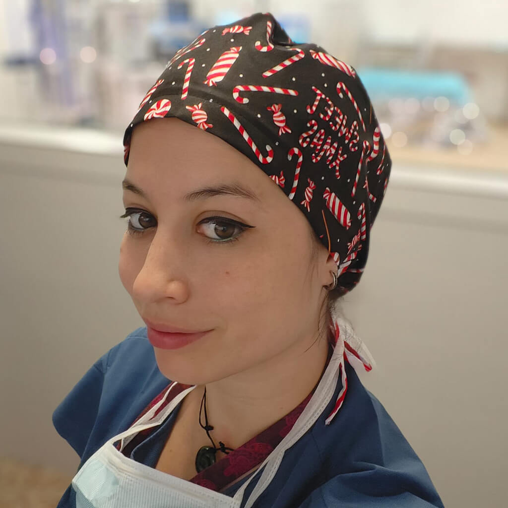 Profesional sanitaria usando gorro quirúrgico SWEET XMAS de Robin Hat con diseño navideño de bastones de azúcar y colores festivos sobre fondo negro, confeccionado en poliéster transpirante para llevar el espíritu navideño durante jornada laboral hospitalaria