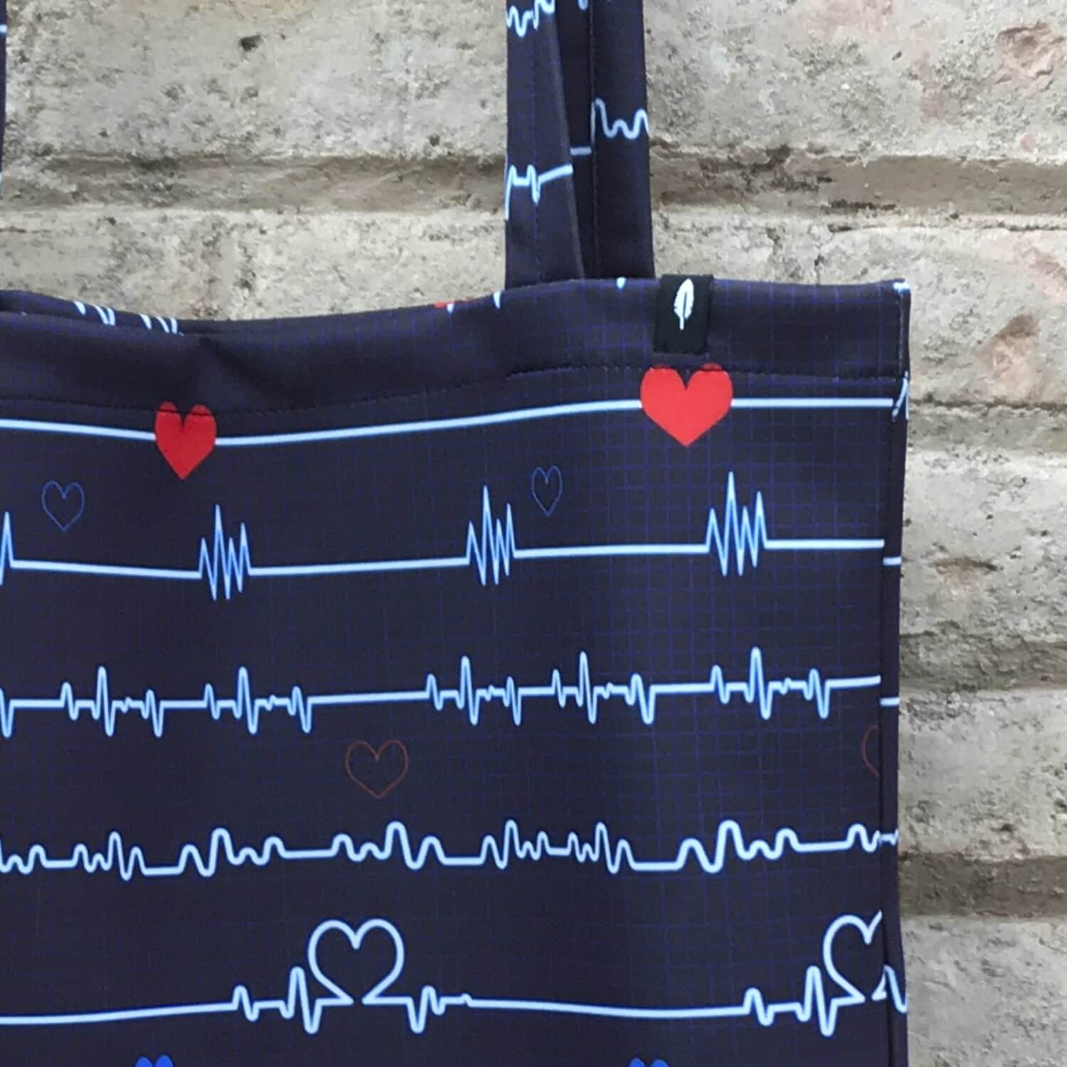 Tote Bag de Robin Hat con diseño de electrocardiograma en fondo azul, en un entorno de uso cotidiano.